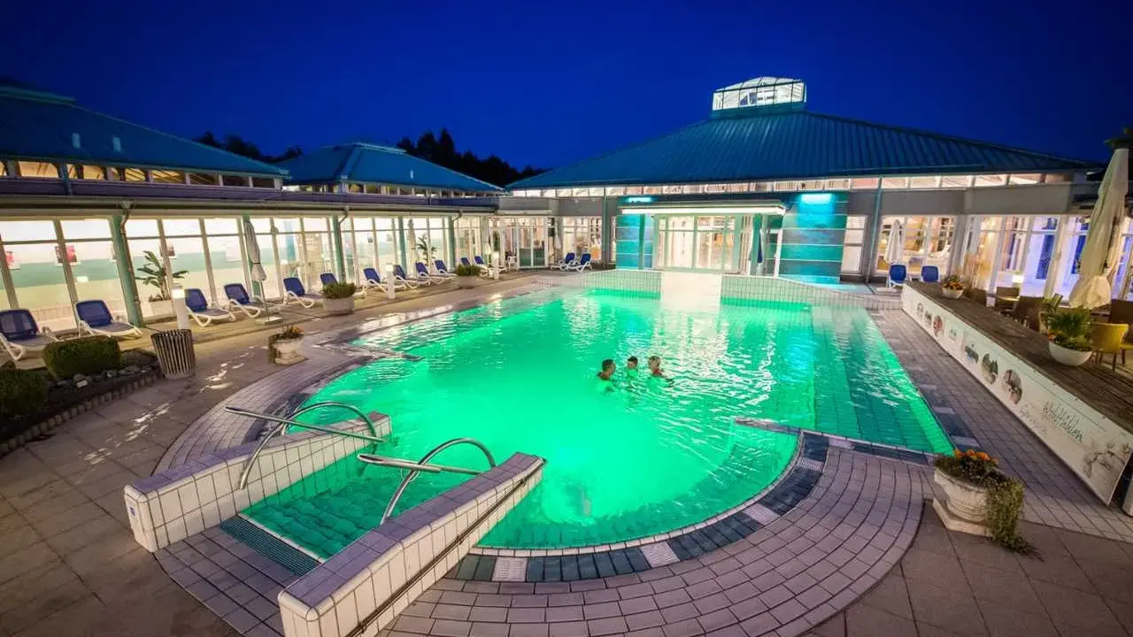 Abendliche Erfrischung im beleuchteten Pool der Therme Bad Driburg. Drei Personen genießen das warme Wasser unter dem klaren Nachthimmel.