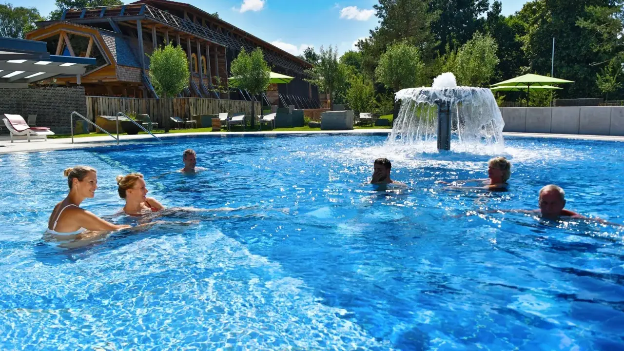 Entspannte Menschen genießen das Schwimmbad eines Kurortes in NRW. Ein Wasserspiel sorgt für Erfrischung.