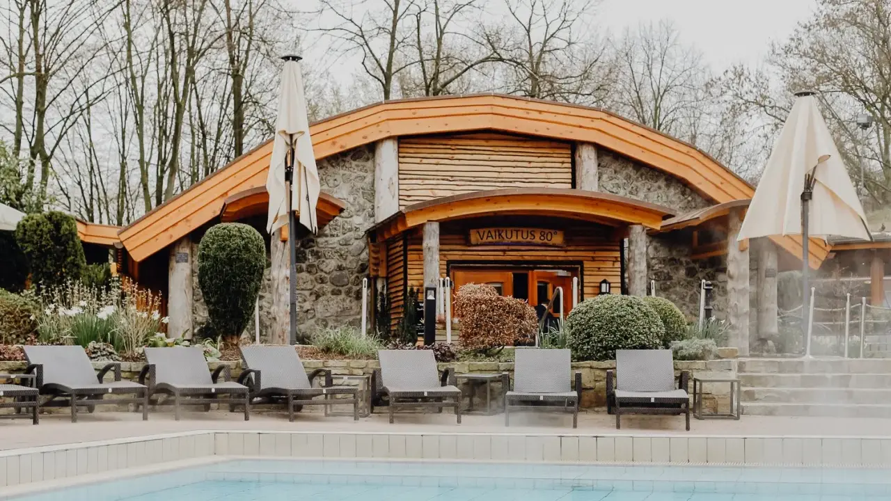 Entspannung am Pool des h2o Herford. Liegestühle laden zum Verweilen ein, während im Hintergrund die Sauna mit der Aufschrift "Vaikutus 80°" lockt.