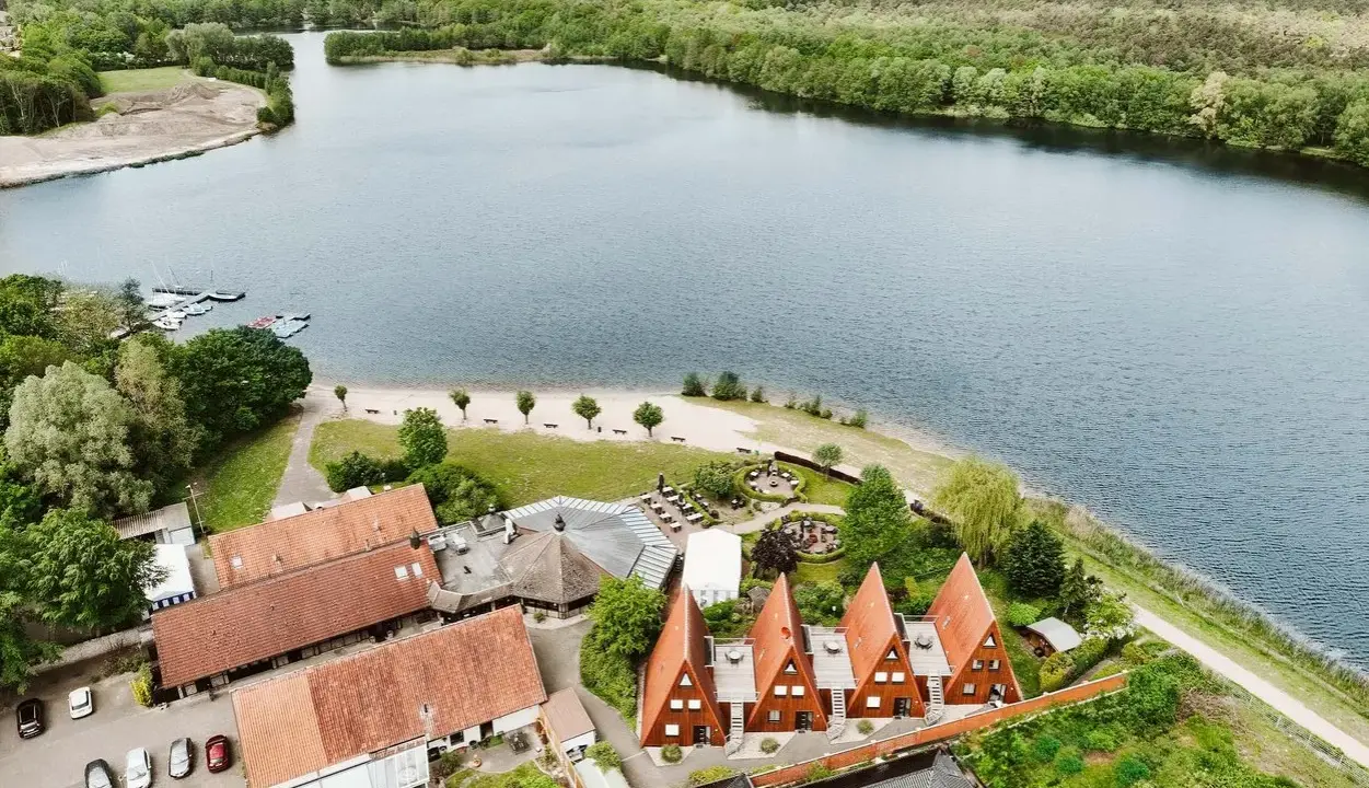 Idyllischer Seeuferbereich mit Sandstrand, Booten und Häusern. Ein perfekter Ort für einen entspannten Seeurlaub in Gronau.