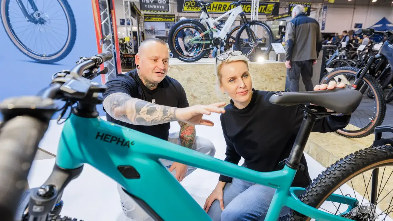 Ein Mann mit Tattoos und eine Frau begutachten auf der Fahrrad Messe ein türkisfarbenes E-Bike.