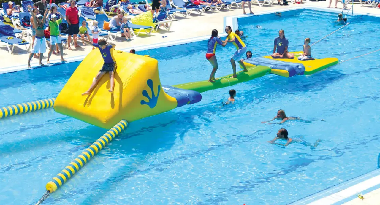 Kinder spielen auf einer aufblasbaren Wasserrutsche und im Pool eines Freibades.