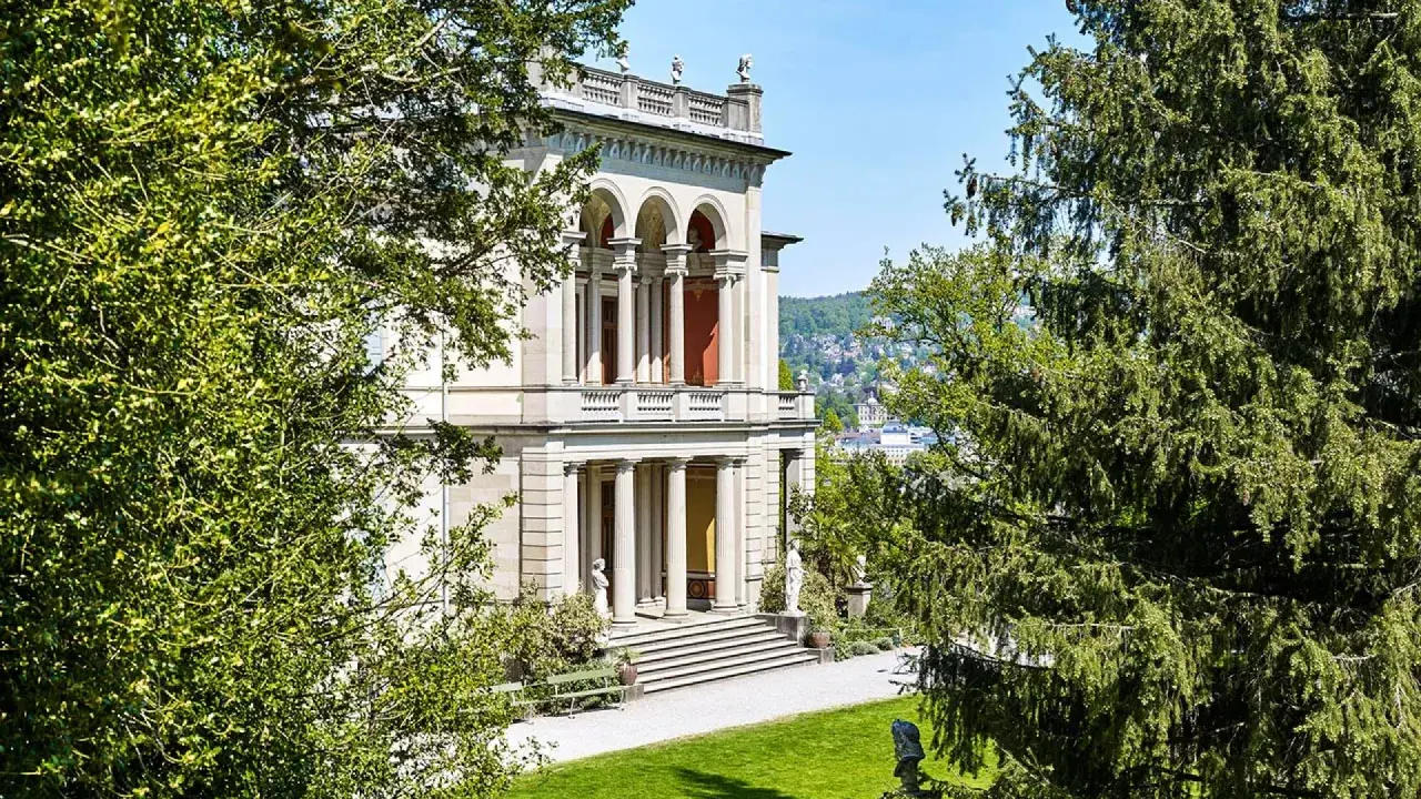Prachtvolles Gebäude mit Säulen und Arkaden, umgeben von grünen Bäumen. Ein schöner Ort, um Kunst zu genießen, wie im Museum Rietberg.