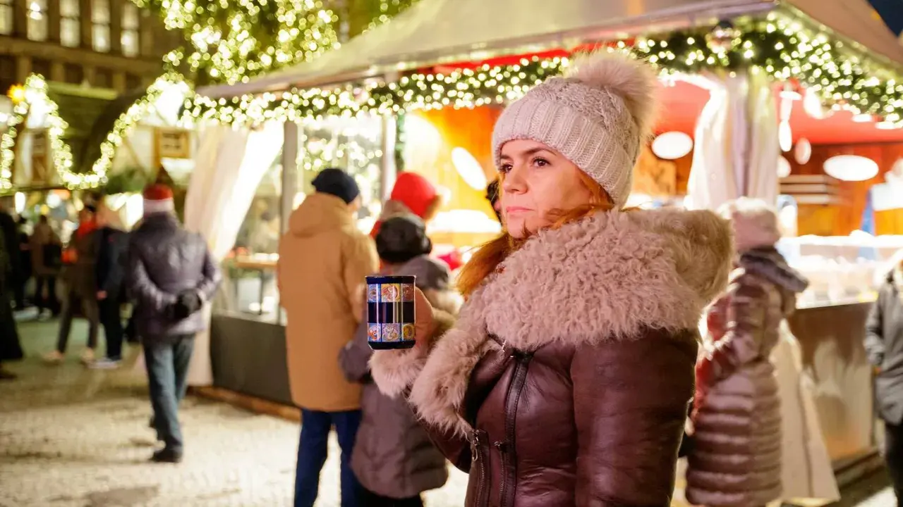 Frau mit Becher auf dem **Weihnachtsmarkt Nottuln**, umgeben von Lichtern und Menschen.