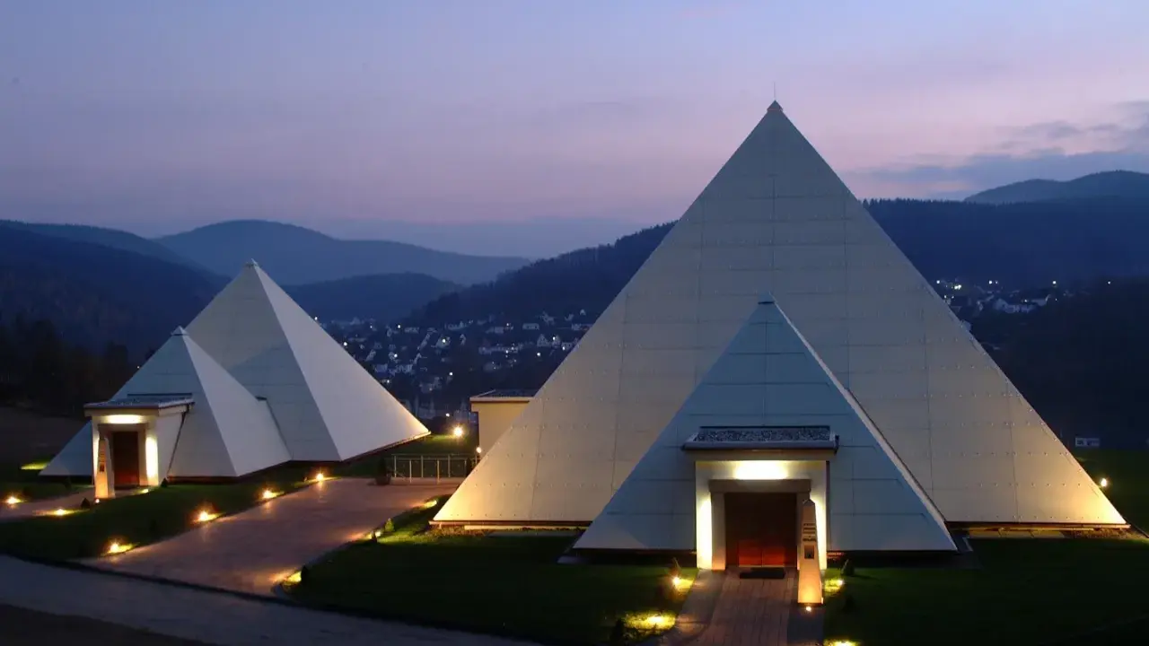 Zwei moderne Pyramiden im Sauerland, beleuchtet im Abendlicht, mit einem Dorf im Hintergrund.