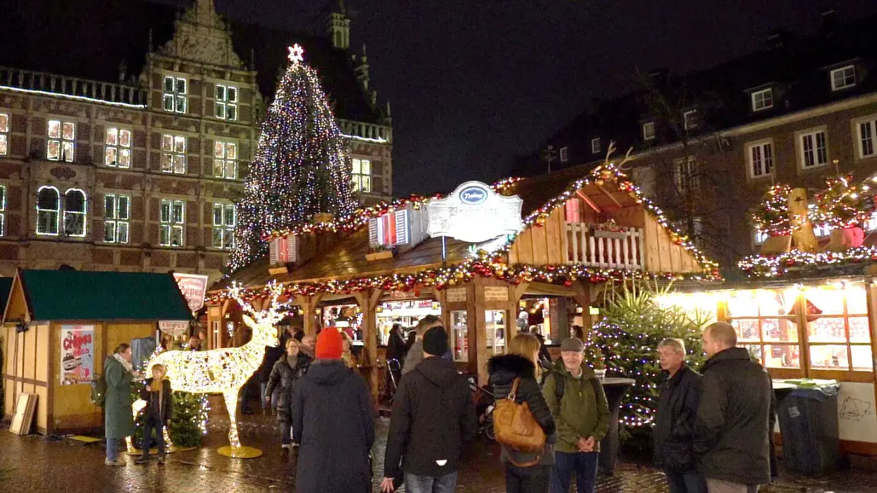 Menschen genießen den festlich beleuchteten weihnachtsmarkt bocholt mit einem großen Weihnachtsbaum und einem Rentier aus Lichtern.