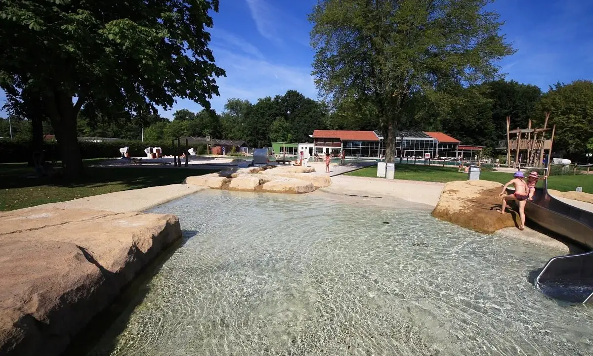 Kinder planschen im flachen Wasser des Parkbad Versmold. Eine Rutsche lockt zum Spielen.