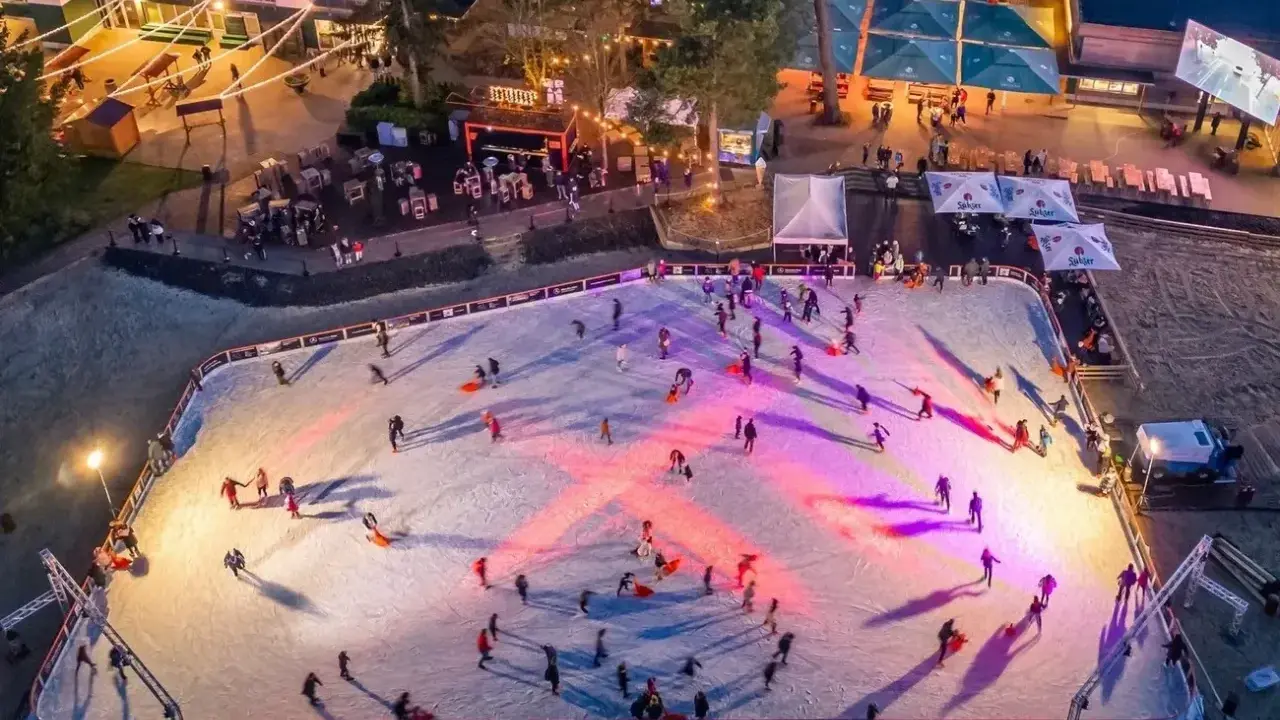 Ein belebter weihnachtsmarkt mit schlittschuhbahn. Menschen gleiten über das Eis, während Lichter die Szene in warme Farben tauchen.
