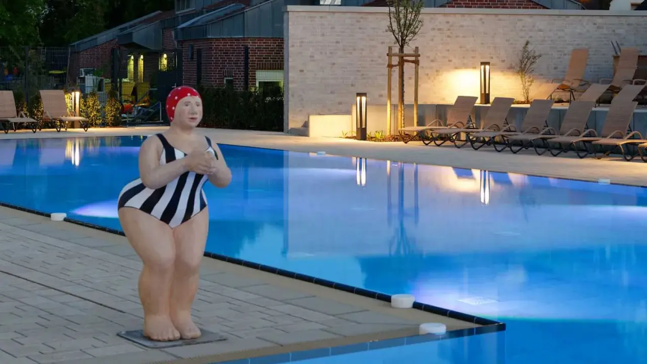 Skulptur einer Schwimmerin am beleuchteten Pool des Solebads Werne. Liegestühle und Bäume säumen das Becken.