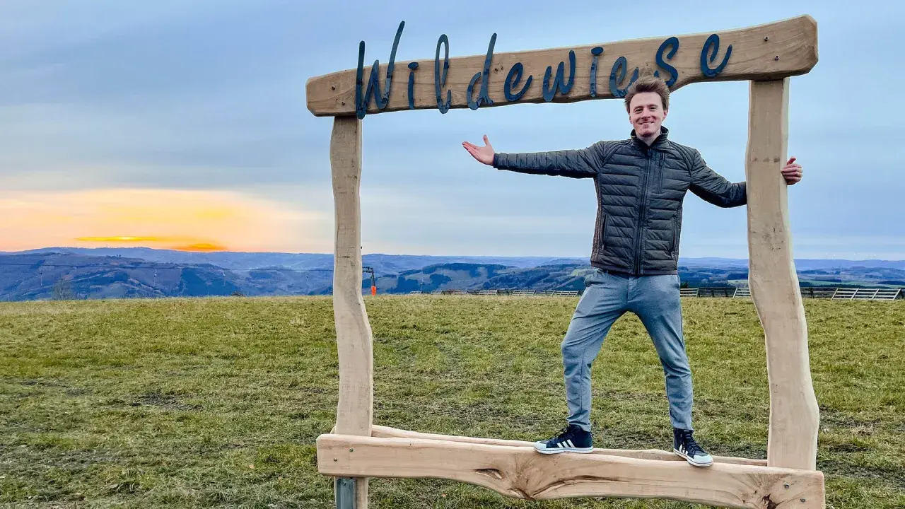 Ein Mann steht vor einem Holzrahmen mit der Aufschrift "Wildewiese". Ein toller Ort für fotospots nrw bei Sonnenuntergang.