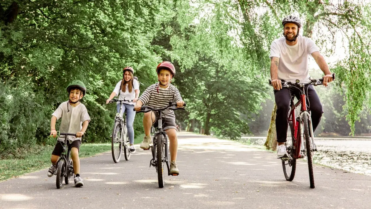Familie genießt eine Fahrradtour mit Kindern in NRW. Vater, Mutter und zwei Jungen radeln auf einem asphaltierten Weg durch eine grüne Allee.