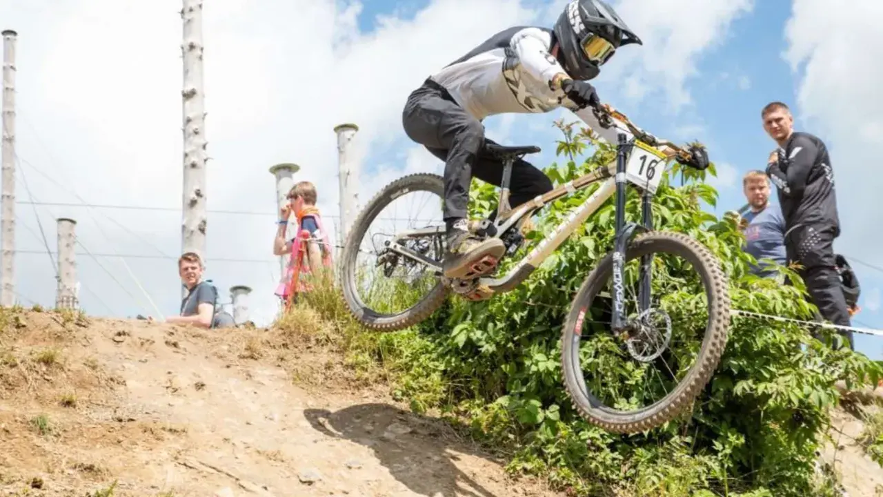 Downhill-Fahrer springt über eine Schanze bei den Dirt Masters Winterberg. Zuschauer beobachten das Spektakel.