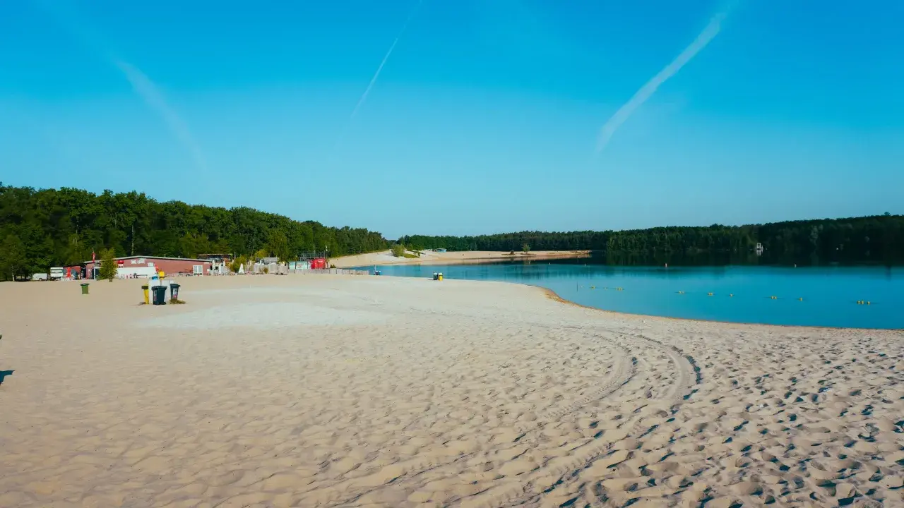 Sonniger Strand in NRW mit feinem Sand, klarem Wasser und grünen Bäumen im Hintergrund. Perfekt für einen entspannten Tag am See.