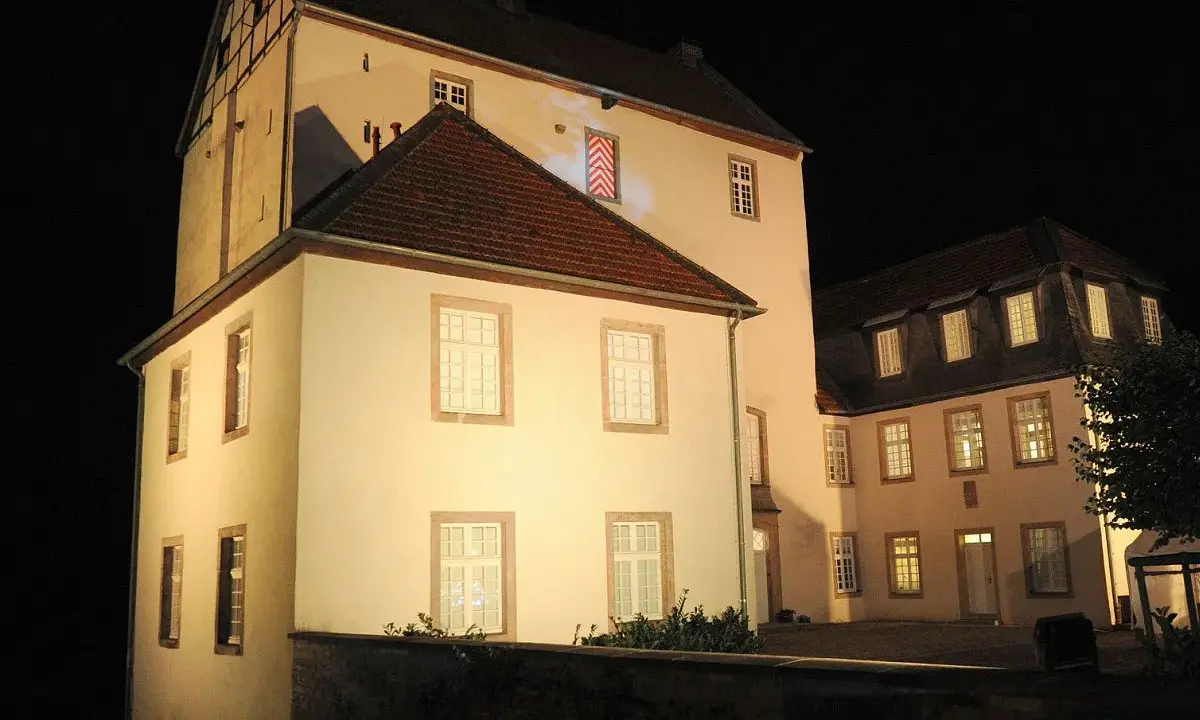 Die beleuchtete Dreckburg in Salzkotten bei Nacht. Ein imposantes Gebäude mit vielen Fenstern und einem dunklen Himmel.