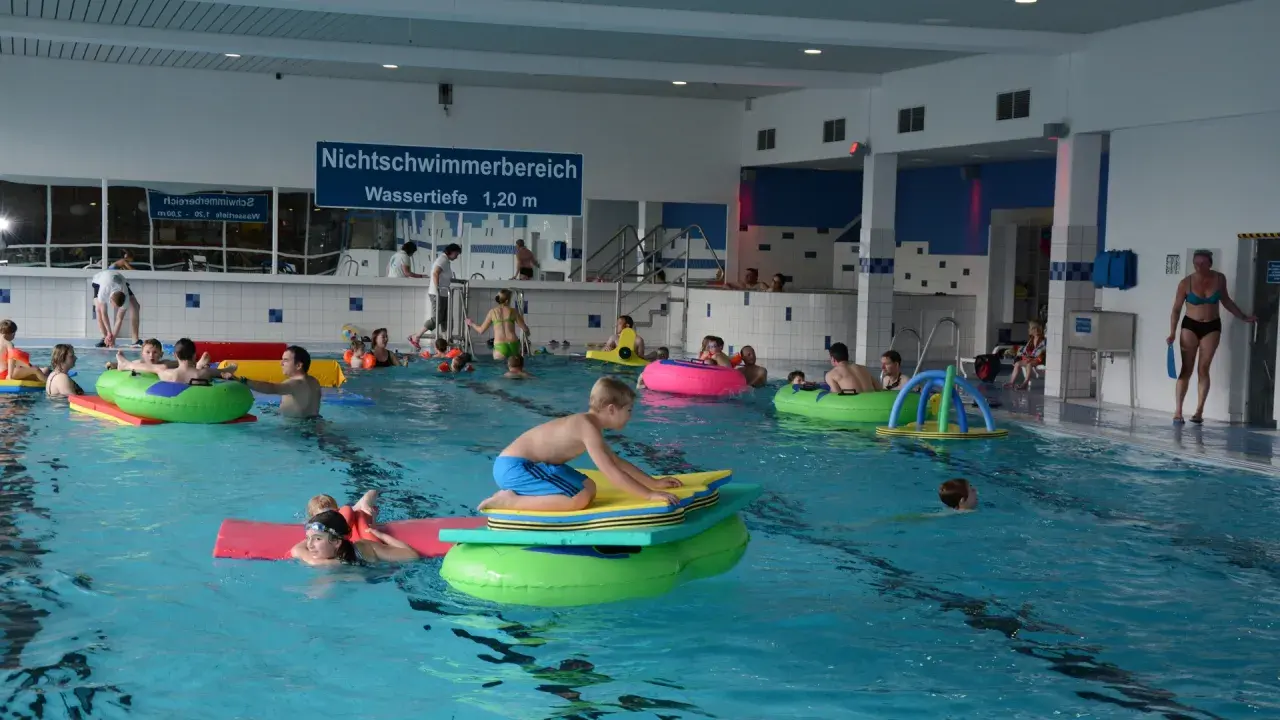 Kinder und Erwachsene planschen im Nichtschwimmerbereich des Schwimmbads Brakel. Viele nutzen bunte Schwimmtiere und Matten.