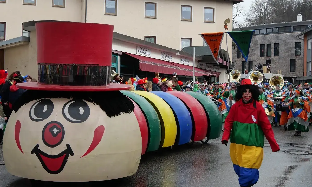 Bunter Karnevalsumzug mit einem riesigen Clown-Motivwagen und kostümierten Menschen. Die Karnevalstage sind voller Freude und bunter Kostüme.