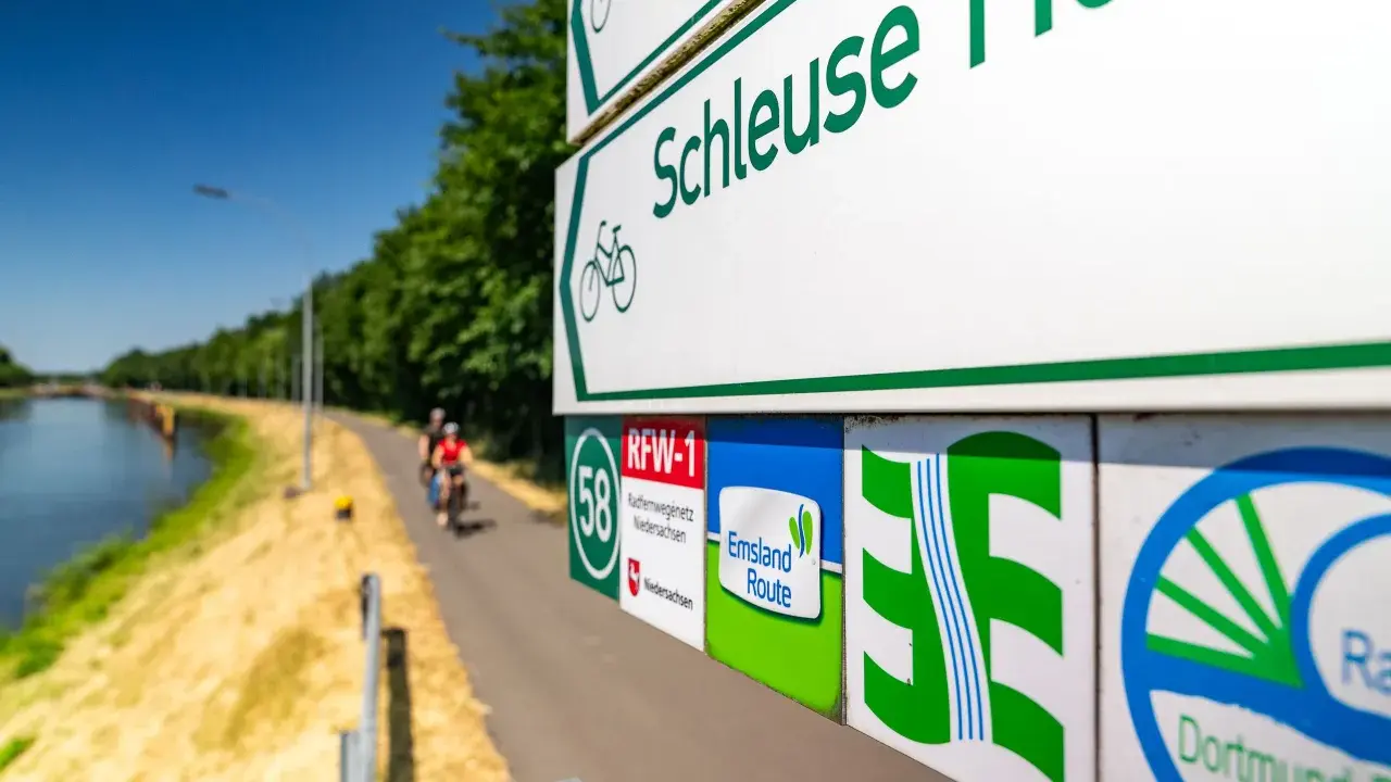 Radwegweiser am Schleusenweg zeigen den Verlauf des Emsland-Radwegs. Radfahrer genießen die Fahrt entlang des Kanals.