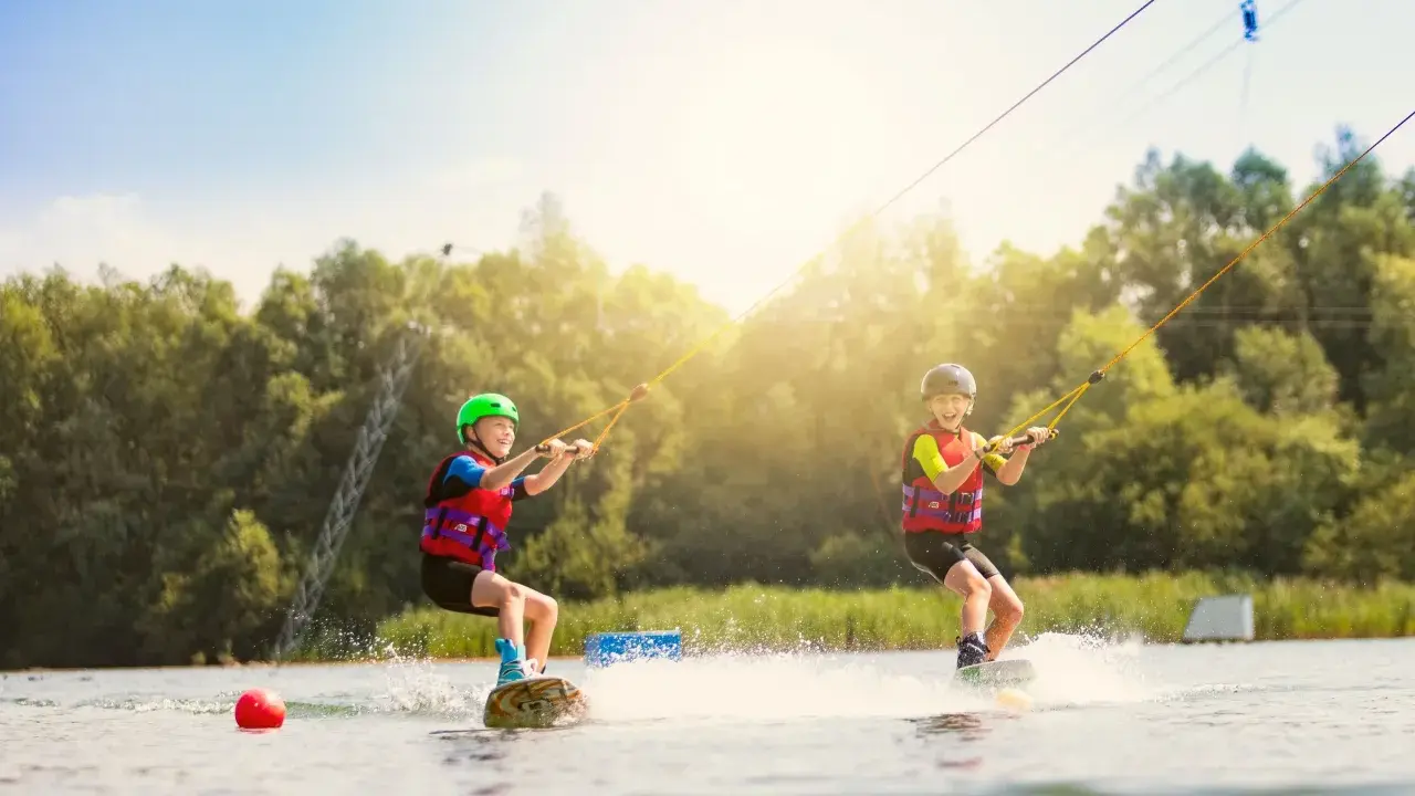 Zwei Kinder üben Wakeboarden am Nesthauser See, gezogen von einer Seilbahn.