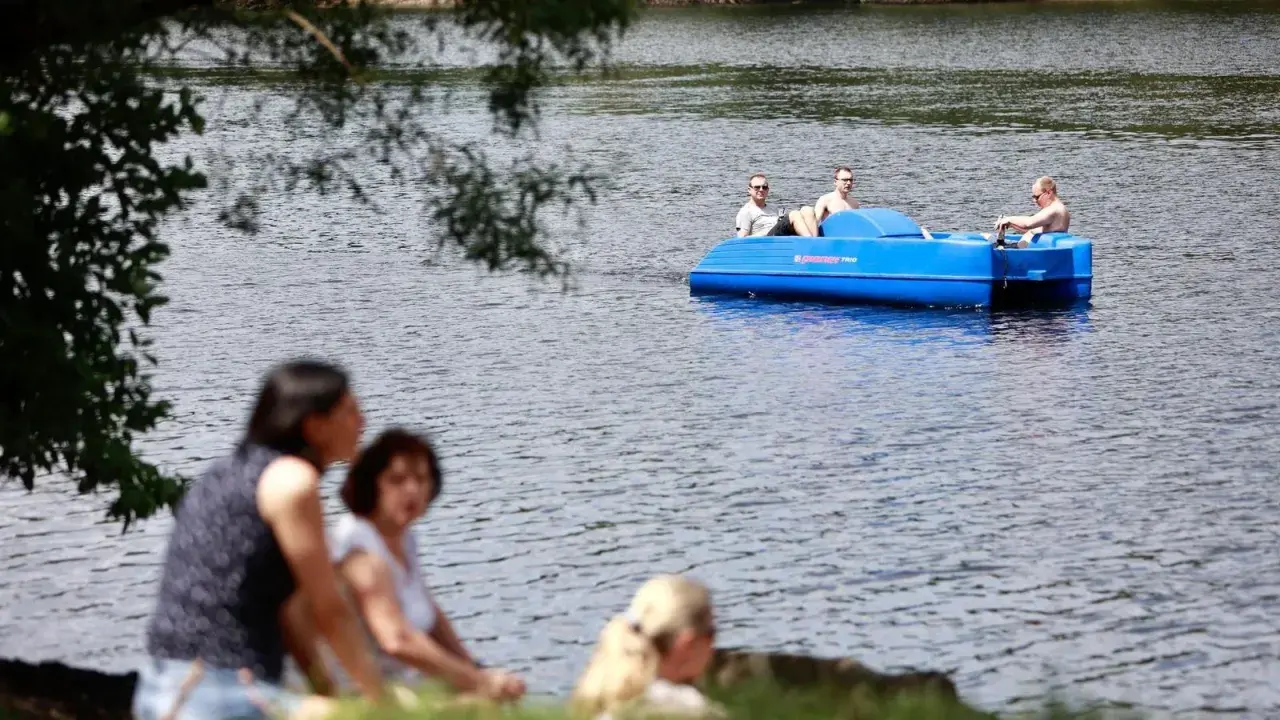 Sommerliche Ausblicke rund um Heiligenhaus: Menschen genießen den Tag am See, während drei Männer in einem blauen Tretboot über das Wasser gleiten.