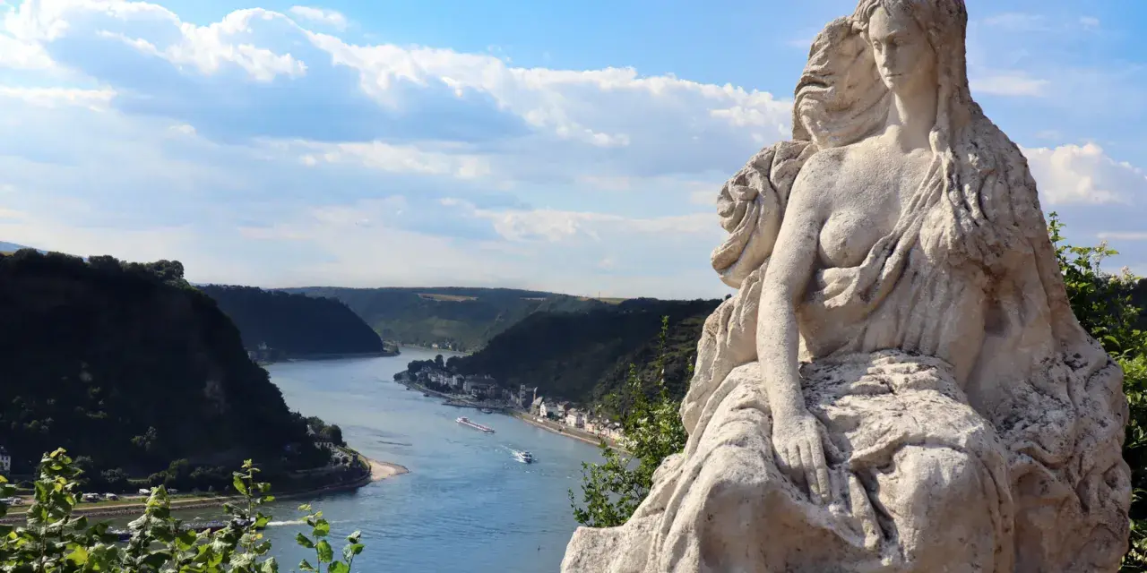 Steinerne Nixe blickt auf den Rhein. Ein malerischer Abschnitt für die Rheinradweg Etappen, mit Schiffen auf dem Wasser und bewaldeten Hängen.