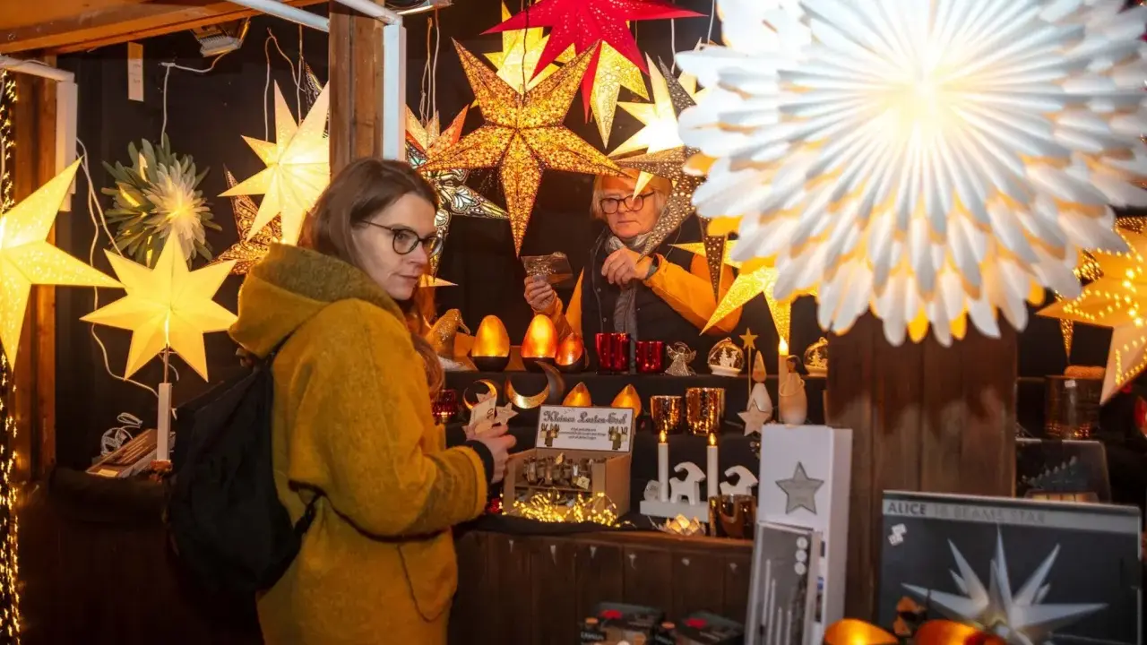 Besucherin auf einem velen Waldweihnachtsmarkt, umgeben von leuchtenden Sternen und weihnachtlicher Deko.
