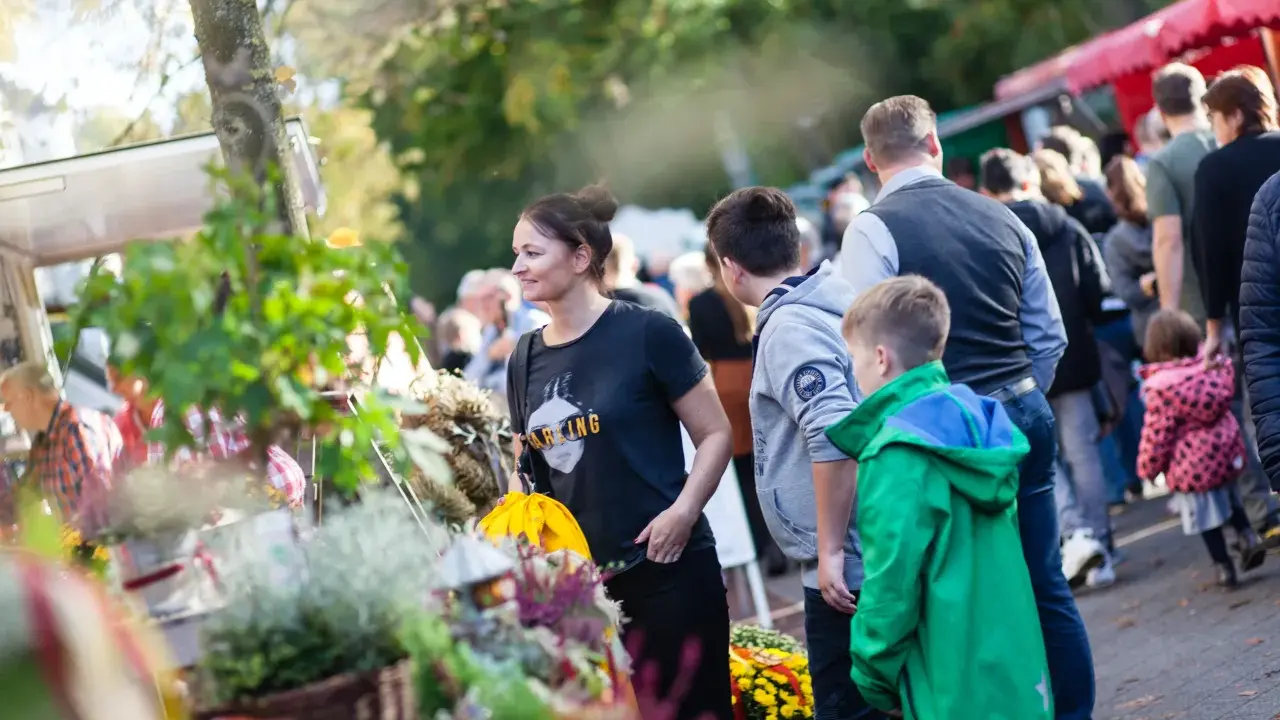 Menschen genießen bunte Veranstaltungen in OWL. Ein Markt mit Blumen und Ständen lockt Besucher an.