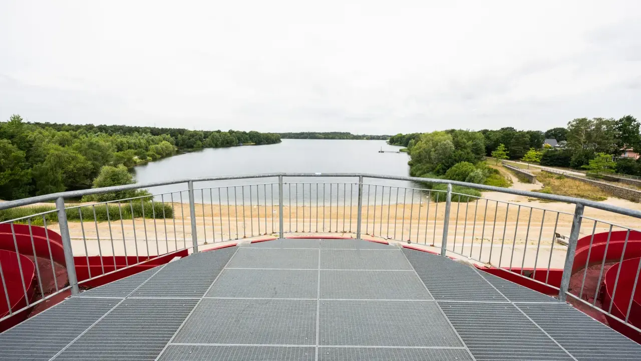 Blick vom Aussichtsturm auf den Offlumer See mit Sandstrand und grünen Ufern.