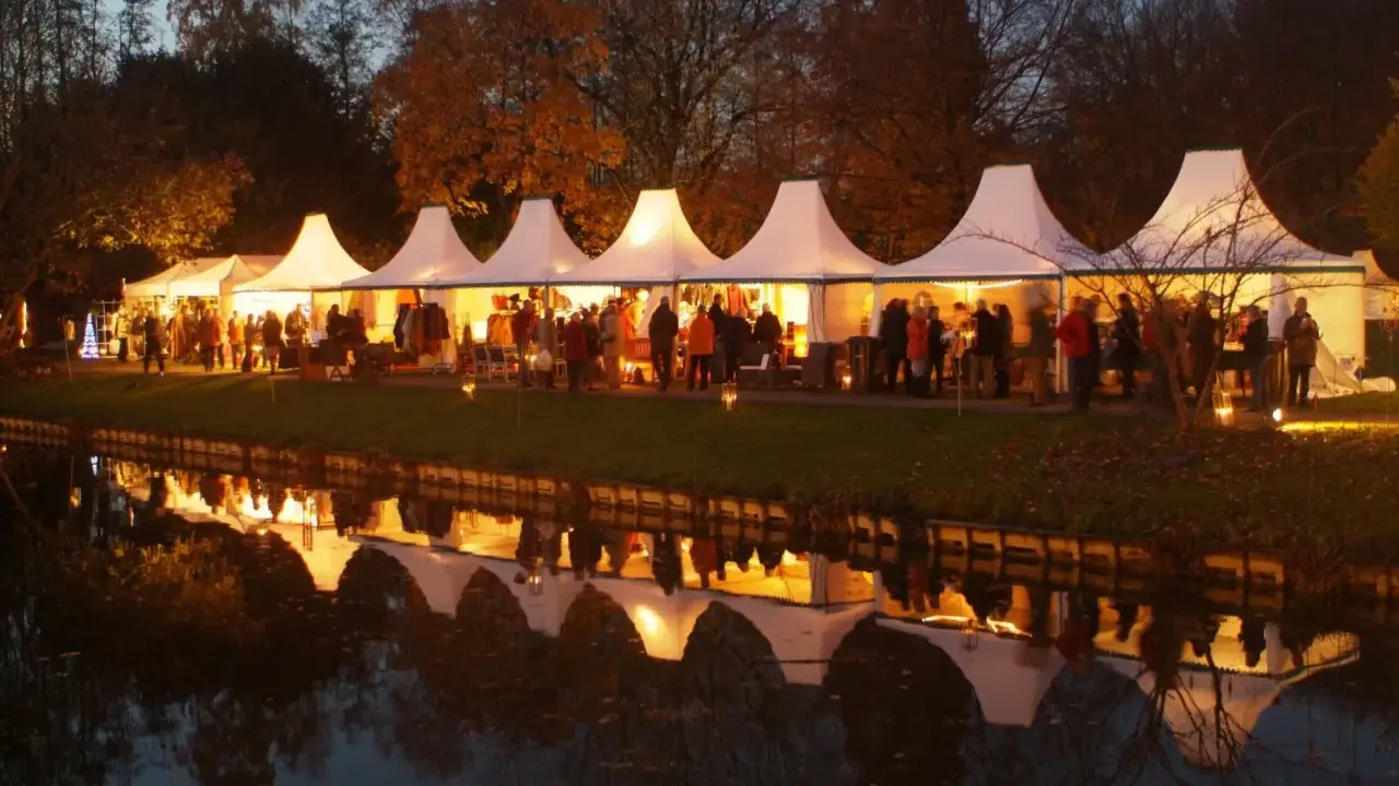 Festliche Zelte am havixbeck weihnachtsmarkt spiegeln sich im Wasser. Besucher bummeln durch die beleuchteten Stände.