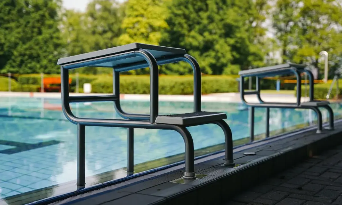 Startblöcke am Beckenrand im Freibad Elverdissen. Das Wasser glitzert, Bäume im Hintergrund.
