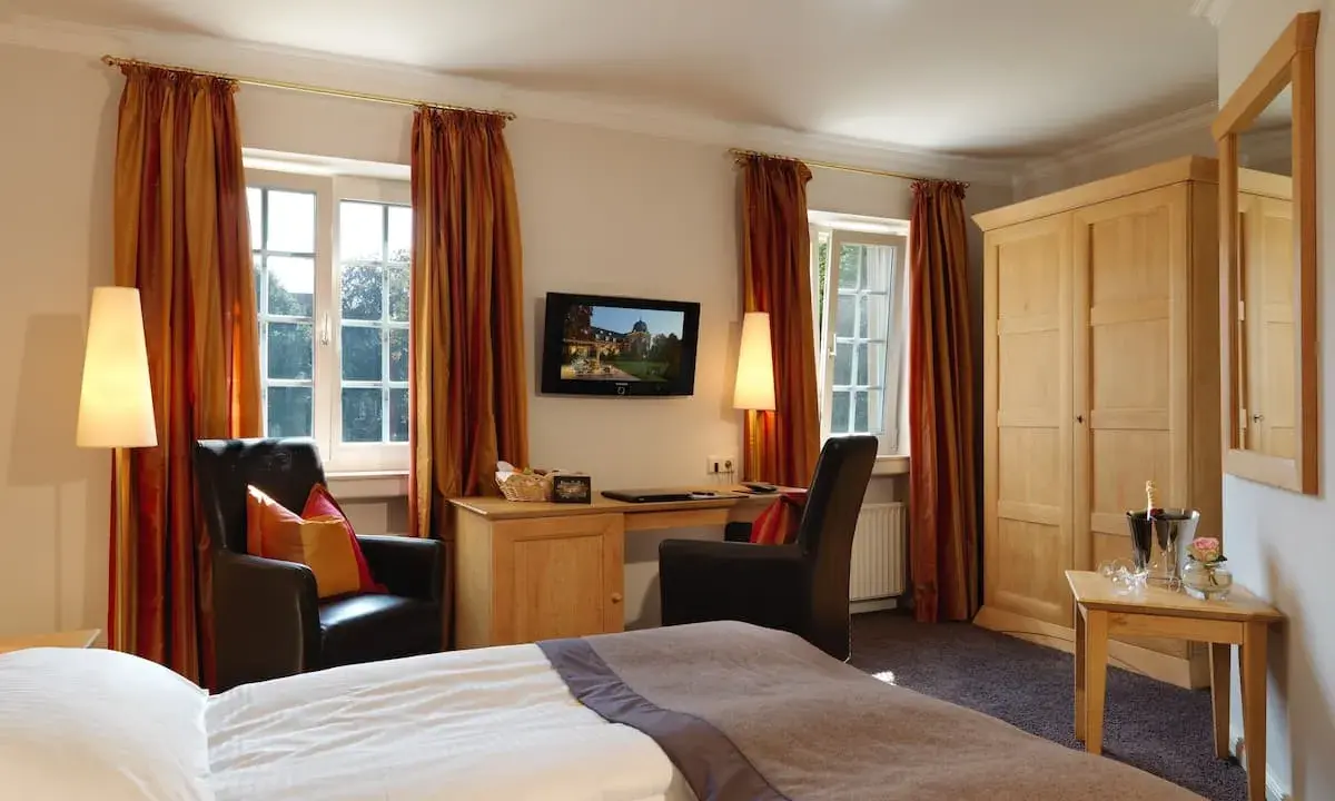 Gemütliches Zimmer mit Blick auf die Klosterpforte Harsewinkel. Einladende Sessel, Schreibtisch und ein großes Bett.