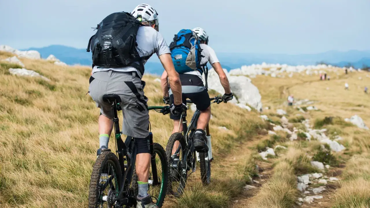 Zwei Radfahrer mit Rucksäcken auf einem Bergpfad. Perfekt für Radreisen und Sternfahrten in der Natur.