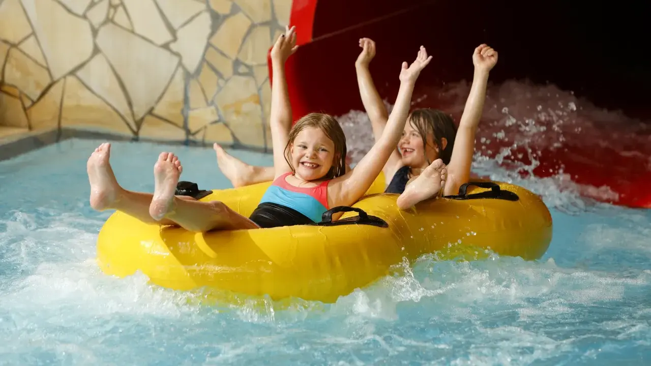 Zwei lachende Kinder rutschen auf einem gelben Schlauchboot durch einen Wasserpark. Ein perfekter Tag, wie ein h2o gutschein!