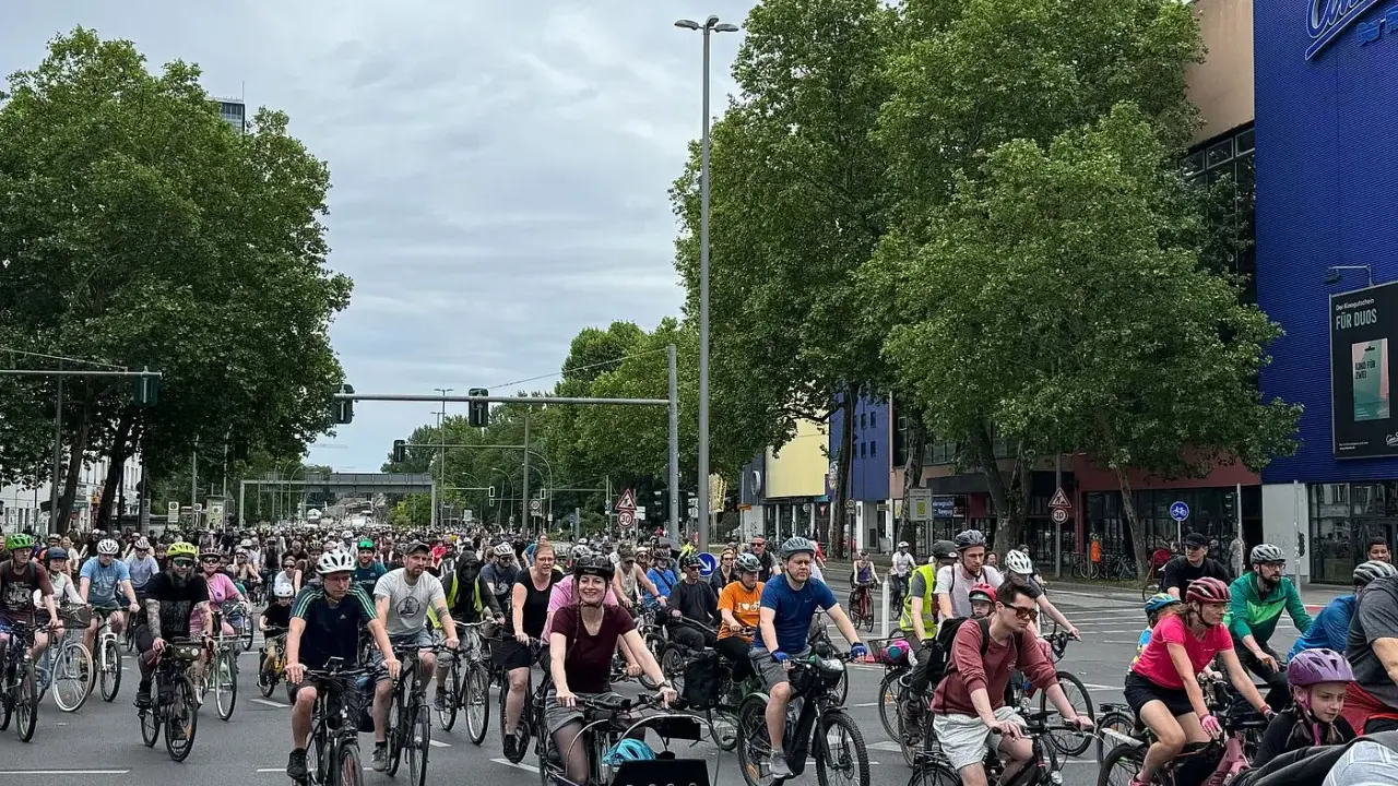 Große Gruppe Radfahrer bei der ADFC Sternfahrt. Viele Menschen auf Fahrrädern fahren auf einer Straße, umgeben von Bäumen und Gebäuden.