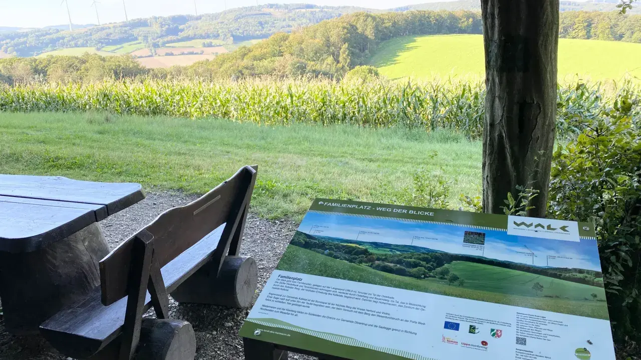 Holzbänke und ein Tisch laden zum Verweilen ein. Ein Schild "Familienplatz - Weg der Blicke" weist auf die Aussicht hin.