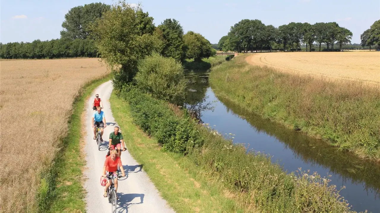 Radfahrer genießen die Fahrt auf dem werse ems radweg entlang eines Kanals und durch Felder.
