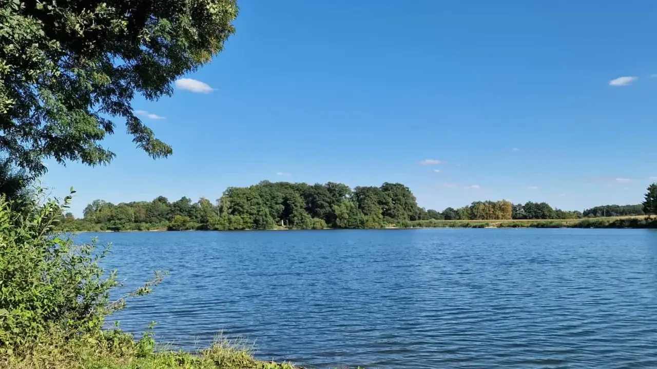 Blauer Himmel über dem ruhigen Linteler See, umgeben von üppigem Grün.