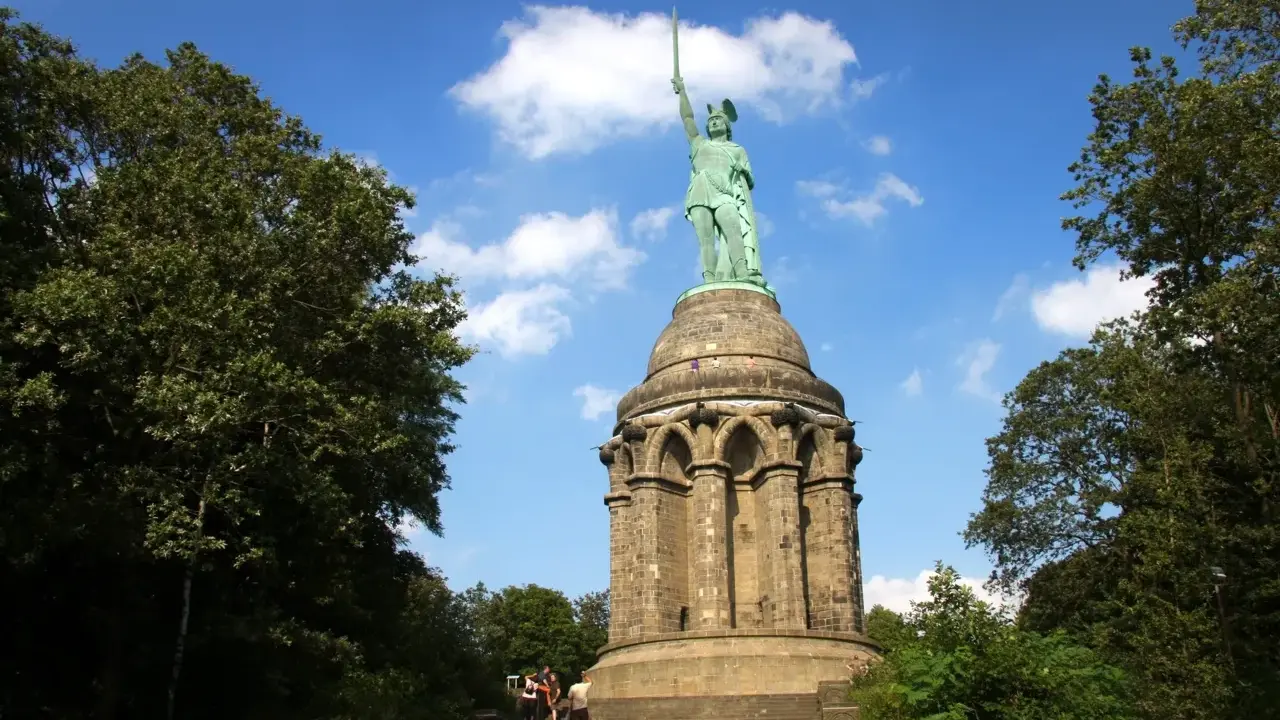 Aufstieg zum Hermannsdenkmal: Wanderer erklimmen die Stufen zum imposanten Reiterstandbild unter blauem Himmel.