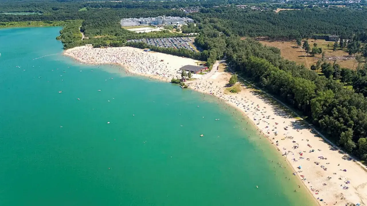 Sonniger Tag am **Silbersee Haltern am See**. Tausende Besucher genießen das türkisfarbene Wasser und den breiten Sandstrand, umgeben von grünen Wäldern.