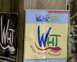 Schilder für die Winterberger Hochtour. Ein Schild zeigt "WHT" in Weiß auf Schwarz, das andere "Winterberg" und "Winterberger Hochtour" in bunten Farben.