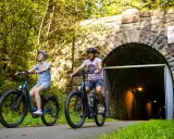 Ein Paar genießt eine entspannte Sauerland Fahrradtour, radelt auf E-Bikes am Eingang des Kuckelheimer Tunnels entlang.