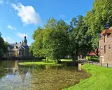 Ein idyllischer vechte radweg führt vorbei an einem Teich, grünen Bäumen und einem historischen Wasserschloss.
