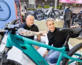 Ein Mann mit Tattoos und eine Frau begutachten auf der Fahrrad Messe ein türkisfarbenes E-Bike.