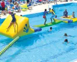 Kinder spielen auf einer aufblasbaren Wasserrutsche und im Pool eines Freibades.