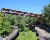 Alte Rohrleitungen der Erzbahntrasse Bochum ragen über üppiges Grün. Ein geschwungener Fußweg schlängelt sich durch die Natur.