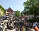 Buntes Treiben auf dem Flohmarkt Minden. Menschen stöbern an Ständen mit Kleidung und Trödel vor Fachwerkhäusern.