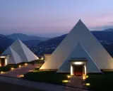 Zwei moderne Pyramiden im Sauerland, beleuchtet im Abendlicht, mit einem Dorf im Hintergrund.