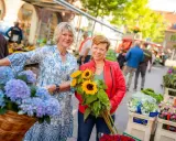 Zwei Frauen mit Blumen auf dem Markt in Coesfeld. Eine hält Sonnenblumen, die andere hat Hortensien im Fahrradkorb.