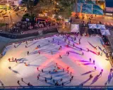 Ein belebter weihnachtsmarkt mit schlittschuhbahn. Menschen gleiten über das Eis, während Lichter die Szene in warme Farben tauchen.