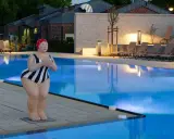 Skulptur einer Schwimmerin am beleuchteten Pool des Solebads Werne. Liegestühle und Bäume säumen das Becken.