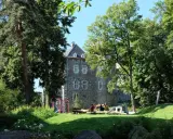 Ein sonniger Tag im Frankenberger Park. Kinder spielen auf einem Spielplatz vor einem alten Gemäuer, umgeben von üppigem Grün.